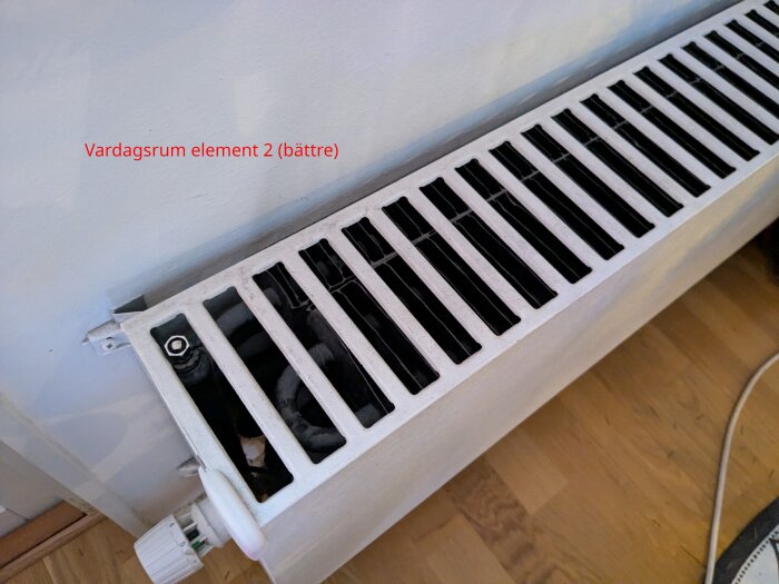 Element i vardagsrum med svartvita spjäll, märkning "Vardagsrum element 2 (bättre)". Synlig termostatventil och anslutningar mot väggen.