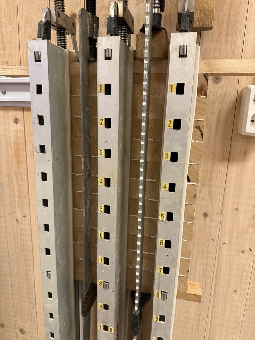 Metallklämor för träbearbetning uppställda mot en trävägg.