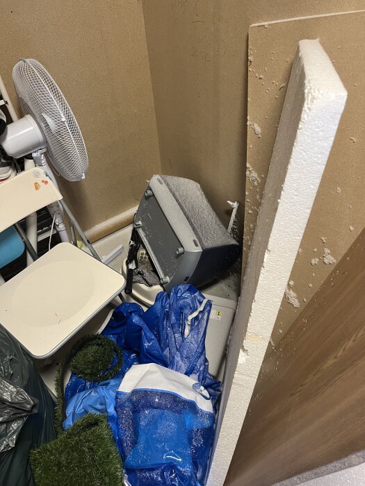 Snö läckt in i ett kallförråd via ventilationshål, täcker en värmefläkt och andra föremål. Blå presenning och hushållsartiklar syns.