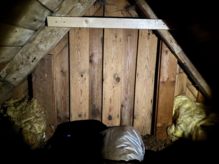 Träpanel på vinden med befintlig isolering på sidorna, ovanligtvis horisontell regel och bruna plankor i mitten, belyst i dämpat ljus.