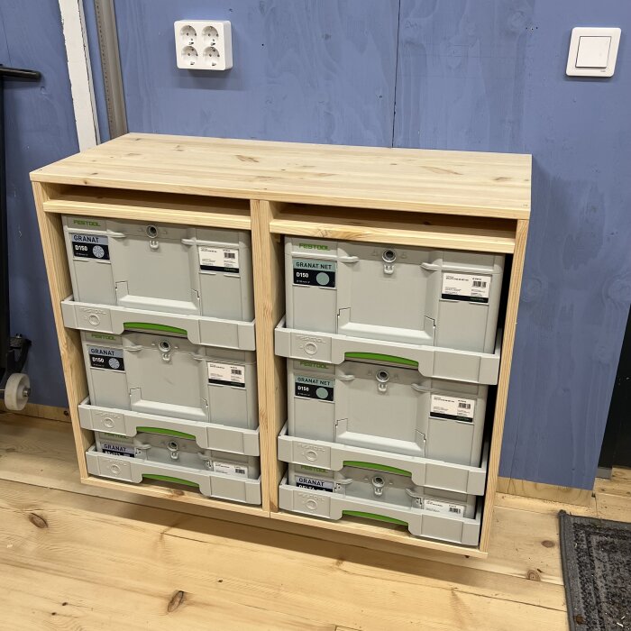 Byrå förvaringslösning med Festool-lådor inbyggda i träställning, stående mot blå vägg och trägolv.