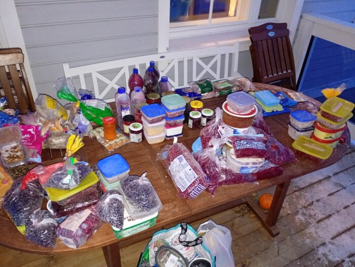 Matvaror och behållare utspridda på ett bord, inklusive bär, sylt och sås i plastpåsar och burkar, för avfrostning och omorganisering av frysen.