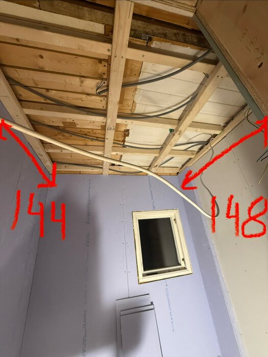 Tak med träbjälkar och exponerade kablar, tre väggar samt fönster synliga. Siffrorna 144 och 148 markerade i rött.