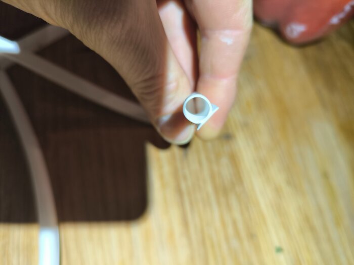 En hand håller i ett vit plastbuntband mot en bakgrund av trä.