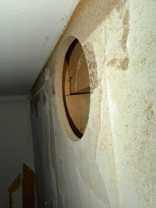 Pyöreä reikä seinässä, josta näkyy puinen rakenne ja tapetti. Seinän tarkoitus määritellään, ei poistettavalle viinikaapin puolelle.