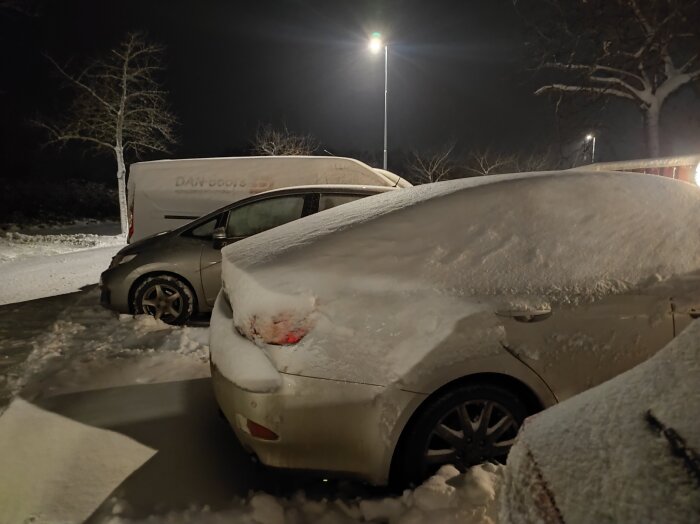 Bil täckt av snö på en parkeringsplats, vilket ger intrycket av en Tesla, på natten under gatubelysning.