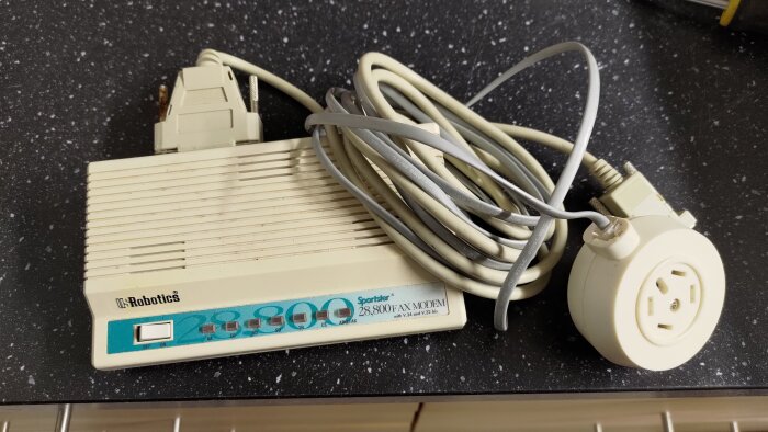 Gammalt modem från US Robotics med kablar på ett svart bord, märkt "Sportster 28,800 Fax Modem".