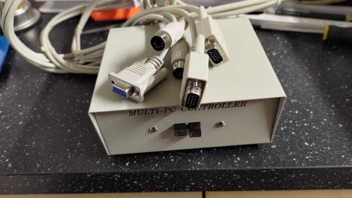 Gammal multi-PC controller med flera anslutna kablar på en svart yta, redo att kastas.