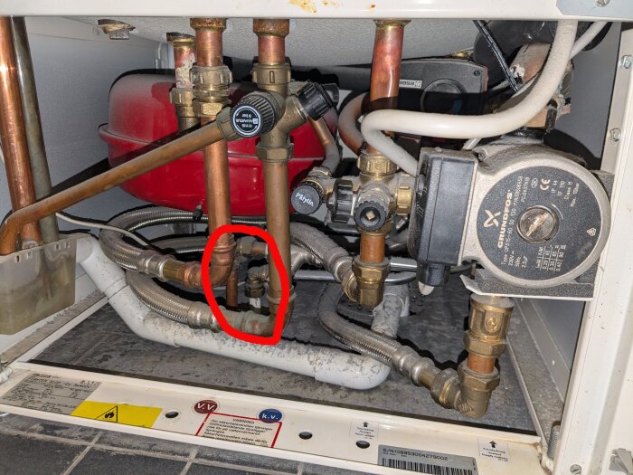 VVS-installation med kopparrör och en cirkulationspump i ett trångt utrymme. En röd expansionstank syns i bakgrunden, ett rör är markerat med rött.