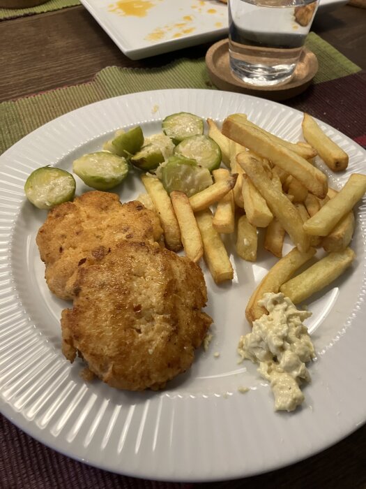 Laxburgare med pommes frites och gratinerad brysselkål på en vit tallrik.