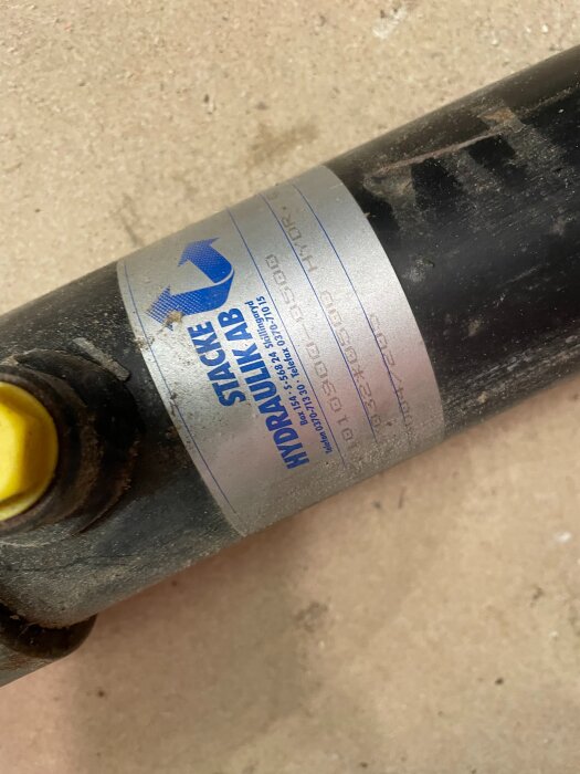Hydraulcylinder med etikett från Stacke Hydraulik AB på en betongyta.