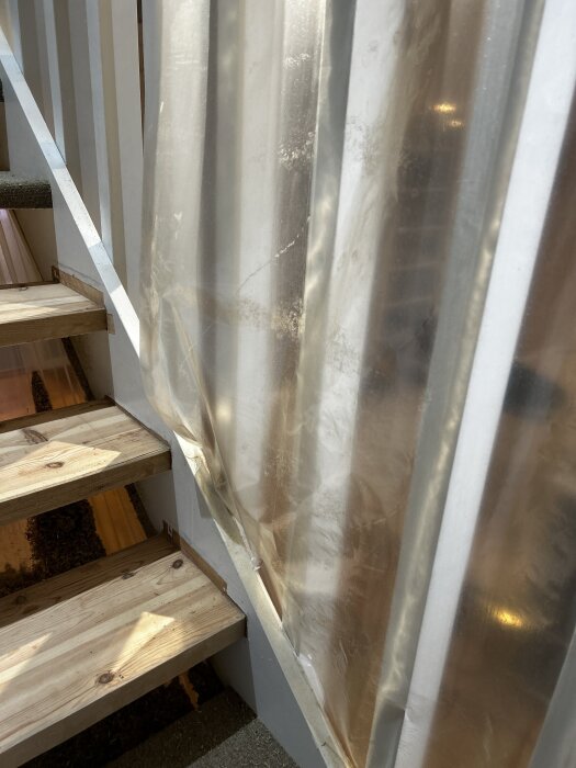 Trappsteg i trä bredvid ett plastskynke som täcker trappräcket under renovering.