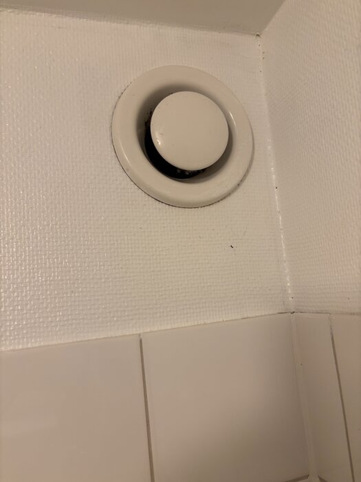Frånluftdon i ett badrumshörn, installerat i vitt kaklat rum.
