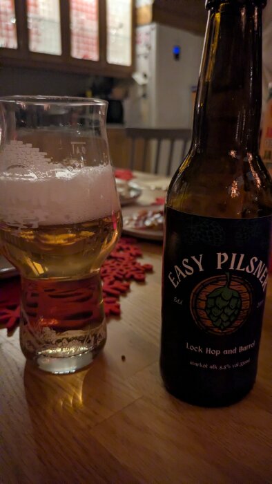 Ölglas och flaska med etiketten "Easy Pilsner" på ett dukat bord.