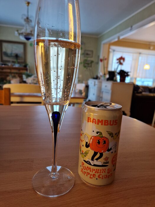 Burk med kryddad äppelcider märkt "Bambus" bredvid ett smalt glas med bubblande cider på ett träbord i ett inomhusrum.