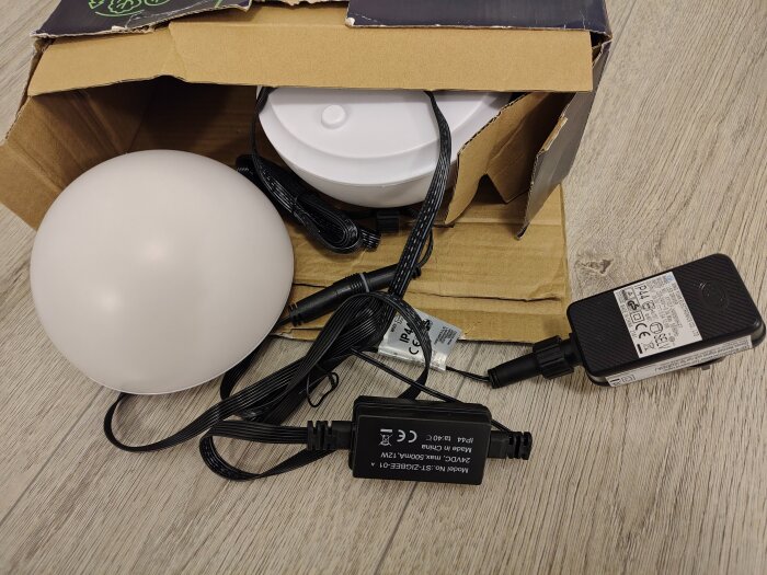 Zigbee 3.0 LED snöboll och tillbehör i kartong på golv, redo för trädgårdsinstallation.