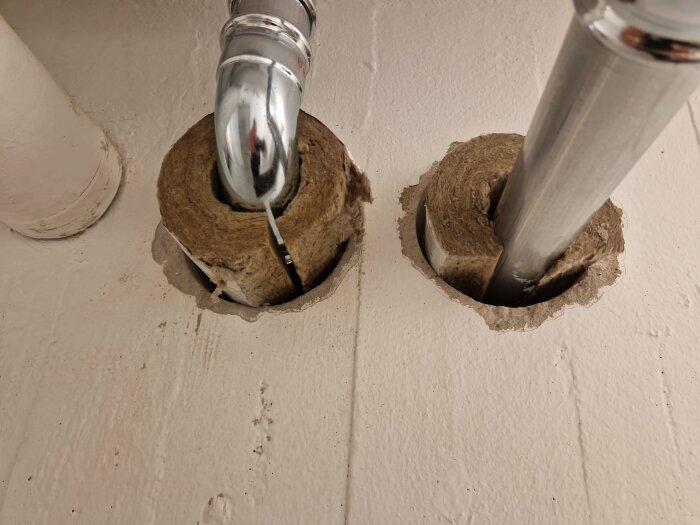 Två rörgenomföringar i en vägg med isolering runt rören, varav ett rör är i krom och det andra i metall.
