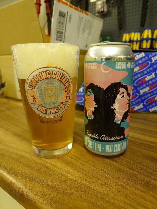 En burk med "Double Attraction" öl och ett fullt ölmugg från Toppling Goliath på ett bord.