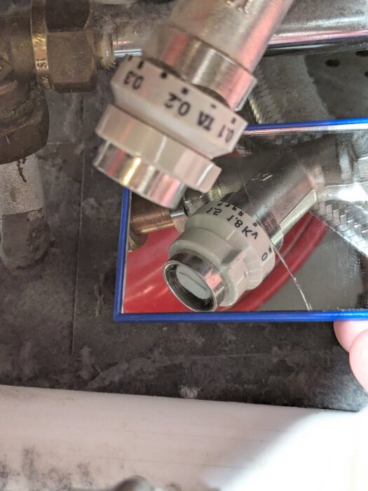 Ett rörsystem med en ventil, där texten "TA" och "1/2" syns på metalldelen. Bilden visar även ett reglage utan pilar.