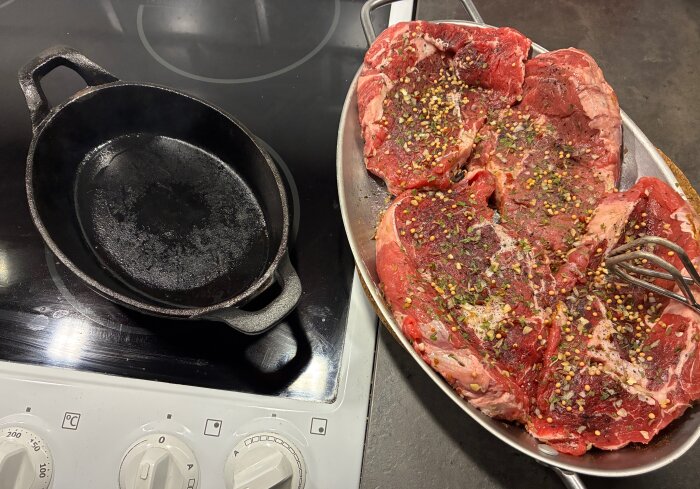 Entrecôte kryddad med örter och peppar ligger bredvid en gjutjärnspanna på spisen, redo att tillagas inomhus istället för utomhusgrillning.