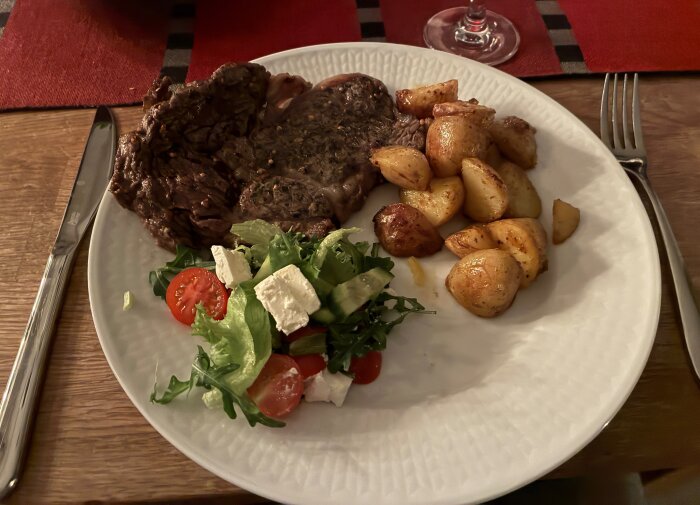 Tallrik med entrecote, kryddiga potatisar och sallad med tomat, fetaost och gurka.