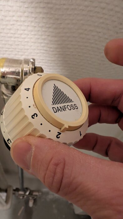 Termostat av märket Danfoss installeras på en ventil på en radiator.