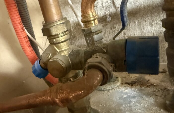 Närbild på ett rörsystem under diskbänken, med kopparledningar och ventiler som är förbundna med plast- och metallkopplingar.