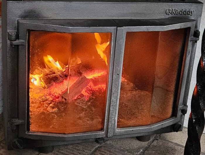 Brasa som brinner i en kamin med glasluckor, sprider varm och lugn atmosfär.
