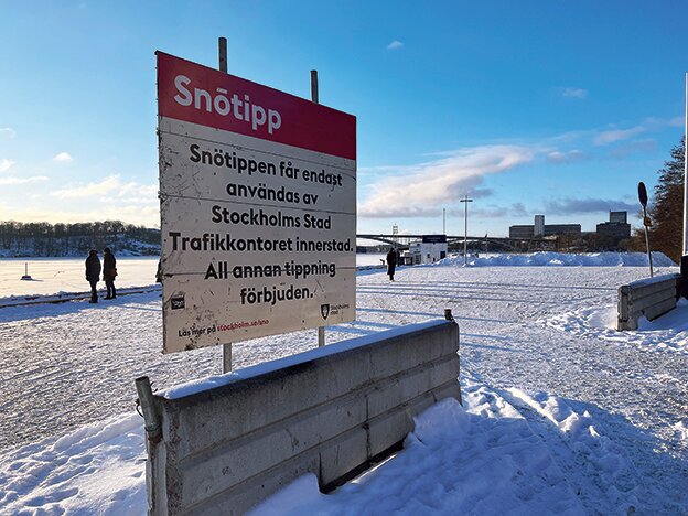 Snötipp-skylt vid en snötäckt väg nära vattnet i Stockholm med människor som går i bakgrunden.