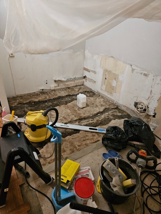 Renovering av ett rum med bortbilad ojämn betong, verktyg och utrustning på golvet inklusive dammsugare och nivåverktyg.