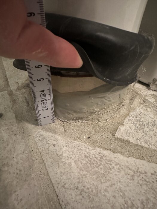 Toalettrör och wc-manschett som mäts med linjal vid byte av gammal toalett. Rör sticker upp 50 mm från golvet.