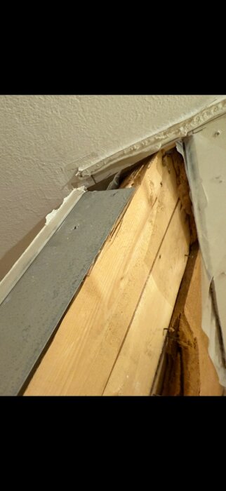 Närbild på en delvis riven vägg med synligt träregelverk och gipsskiva i ett renoveringsprojekt av ett hus på övervåningen.