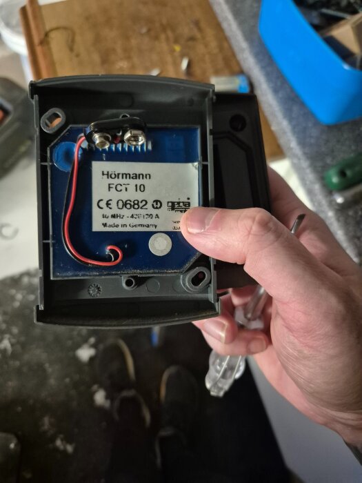 Närbild av ett gammalt Hörmann FCT 10 kodlås utan batteri, med synlig märkning och kablar. Personen håller låset i handen.