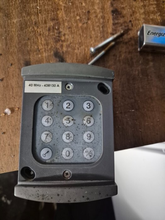 Gammalt Hörmann 40 MHz kodlås på träbord, siffror och nyckelsymbol synliga, skruvar och batteri bredvid.