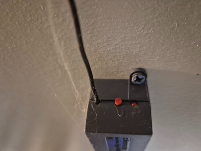 En närbild av ett svart kodlås från Hörmann med en synlig skruv och sladd mot en vit vägg.