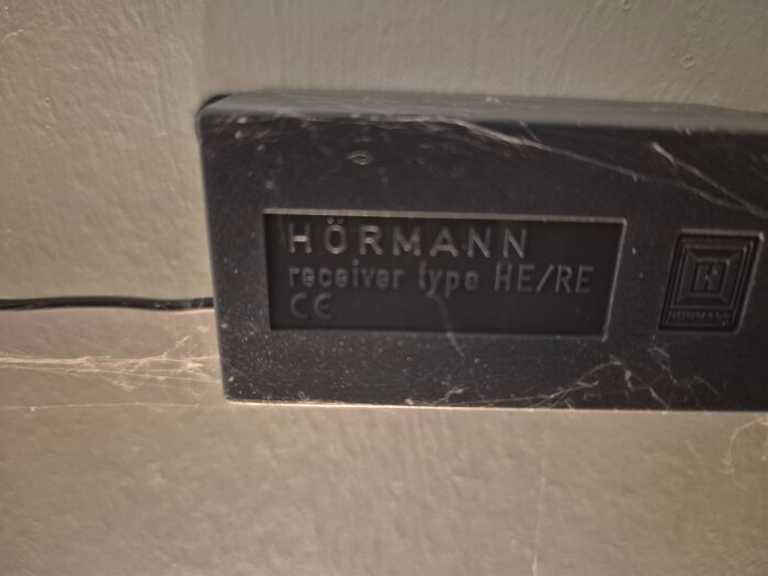 Hörmann mottagarenhet HE/RE monterad på en vägg, med synlig etikett och kabel.