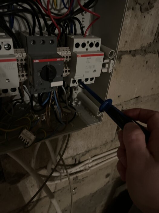 En person använder en spänningsdetektor för att testa en brytare i en elektrisk kopplingslåda på en vägg.