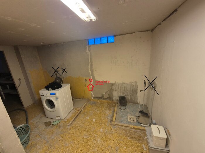 Tvättstuga under renovering med en tvättmaskin, markerade områden på väggen och golvet, och rör under arbete för ny vattenfördelning.