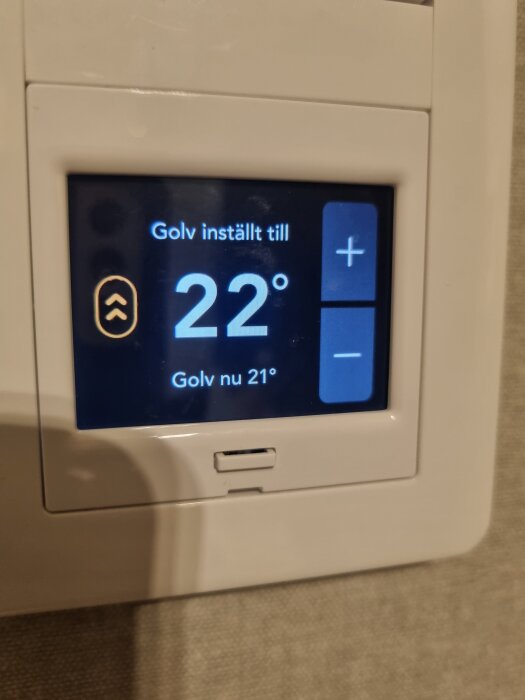 Termostat visar att golvet är inställt till 22°C och aktuell temperatur är 21°C, monterad på en vägg.