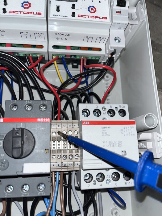 Elektrisk kopplingsbox med kablar och en skruvmejsel pekande på en terminal.