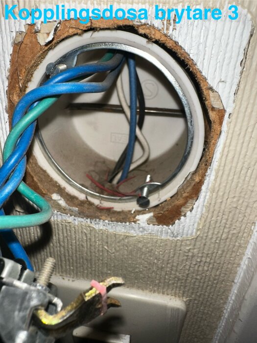 Kopplingsdosa med flera färgade elkablar synliga, inklusive blå och gröna, för anslutning av dimmer till brytare i en korridor.