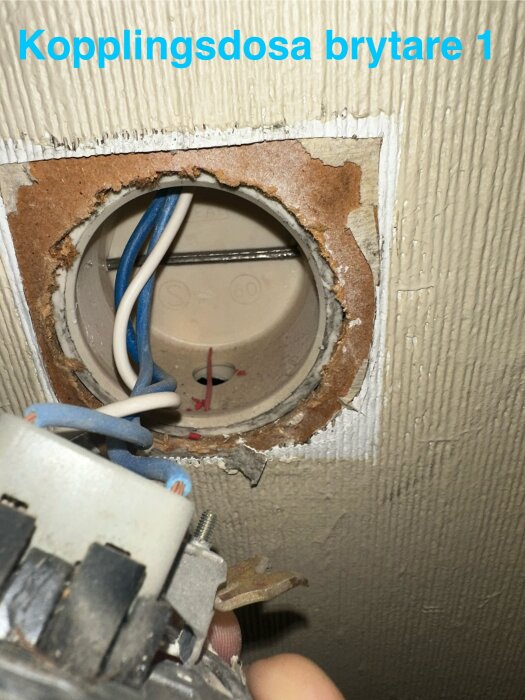 Kopplingsdosa med elektriska kablar och en blått och vitt trådpar synligt, samt en demonterad brytare i förgrunden.
