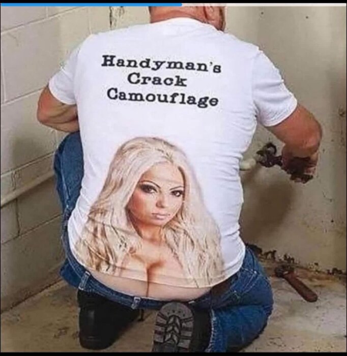 En man i en humoristisk t-shirt med texten "Handyman's Crack Camouflage" och bild på en kvinna, hukar sig vid ett rör.