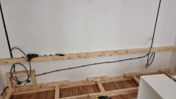 Träram för platsbyggd hylla och vägghängd TV med dolda kablar under renovering i vardagsrum.