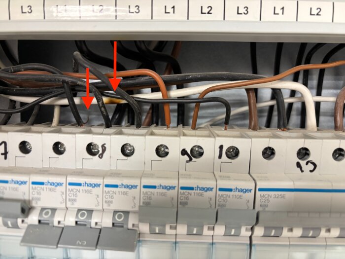 Elcentral med flera kablar; en kardel sticker ut vid L1 i grupp 8 och en vit kabel vid L3 i grupp 13 visar brännskador, markerad med pilar.