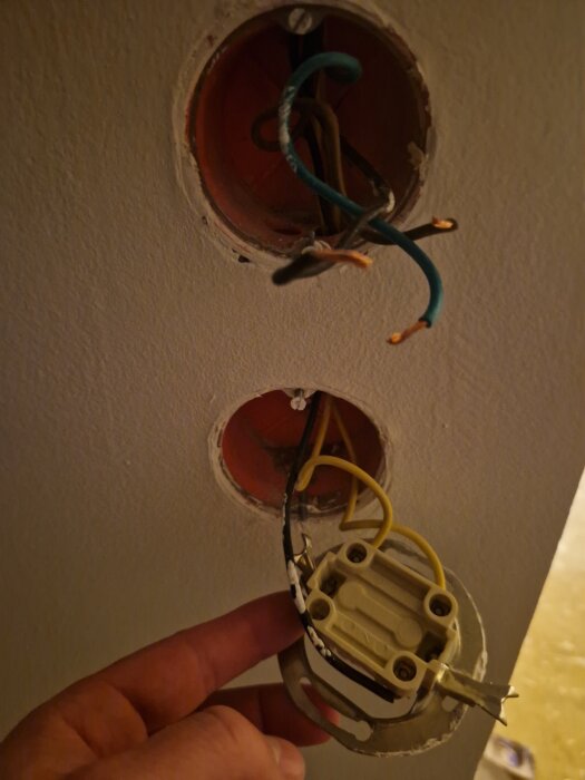 Vägguttag med synliga elkablar och en hand som håller en kronbrytare, visas i en lägenhet under renovering.