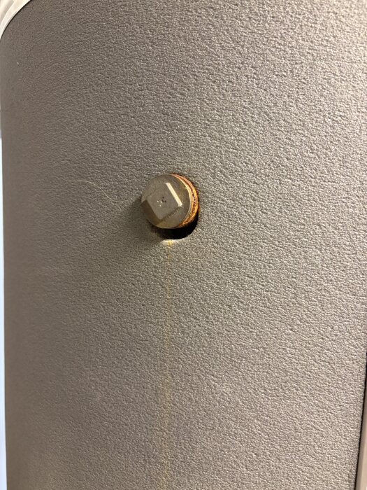 Närbild av skruv på varmvattenberedare med rostmissfärgning runt skruven och nedåt.