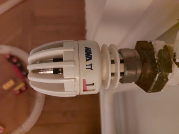 Termostatventil på uppvärmningselement, märkt med "MMT1", monterad på ett rör med lite ytlig korrosion.