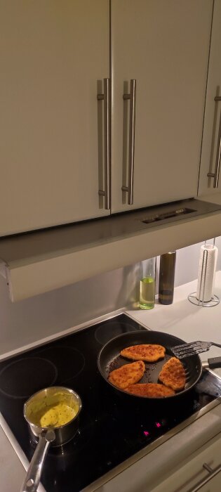 Utdragbar köksfläkt från Bosch över en spis, med en stekpanna och en kastrull på spishällen. Fläkten är nästan helt intryckt.