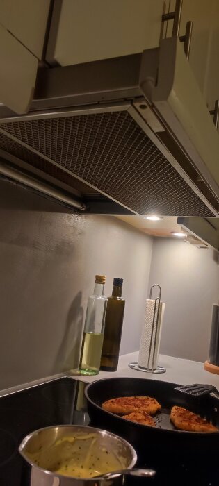 Utdragbar köksfläkt från Bosch ovanför spis med matlagning, fläkten delvis utdragen.